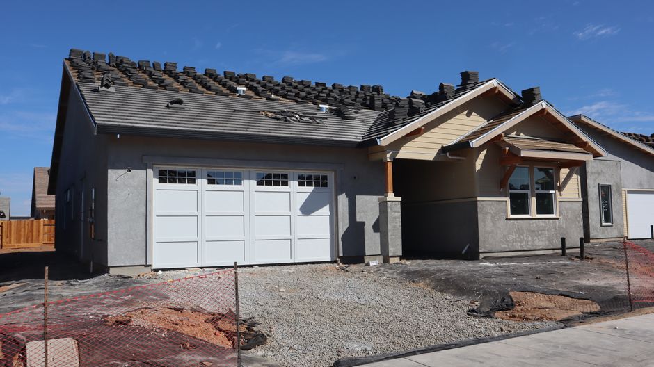 Modern suburban home under construction showcasing roof tiles being installed against a clear sky.
